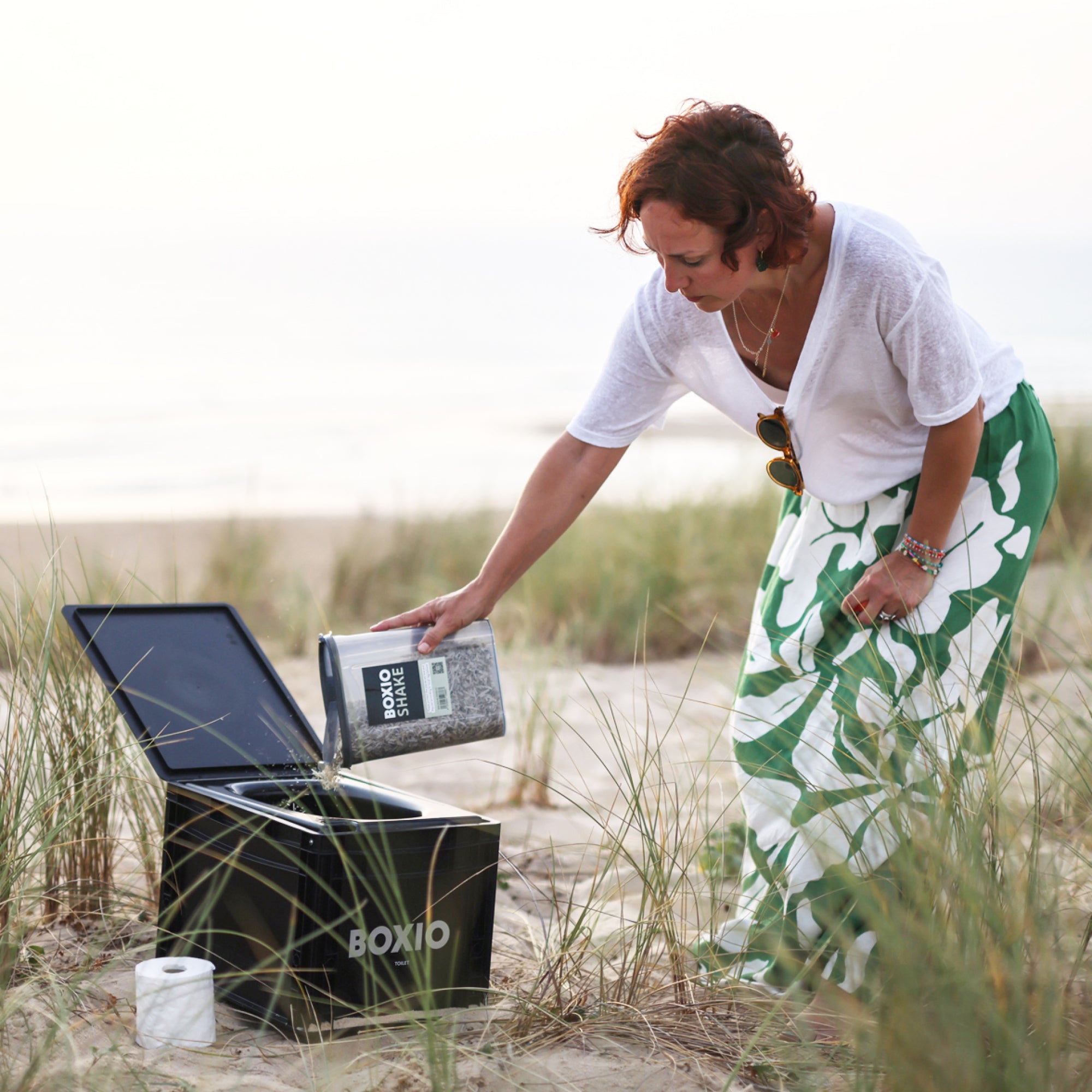 Person using the BOXIO portable bathroom system on the beach, showcasing convenience and outdoor functionality.