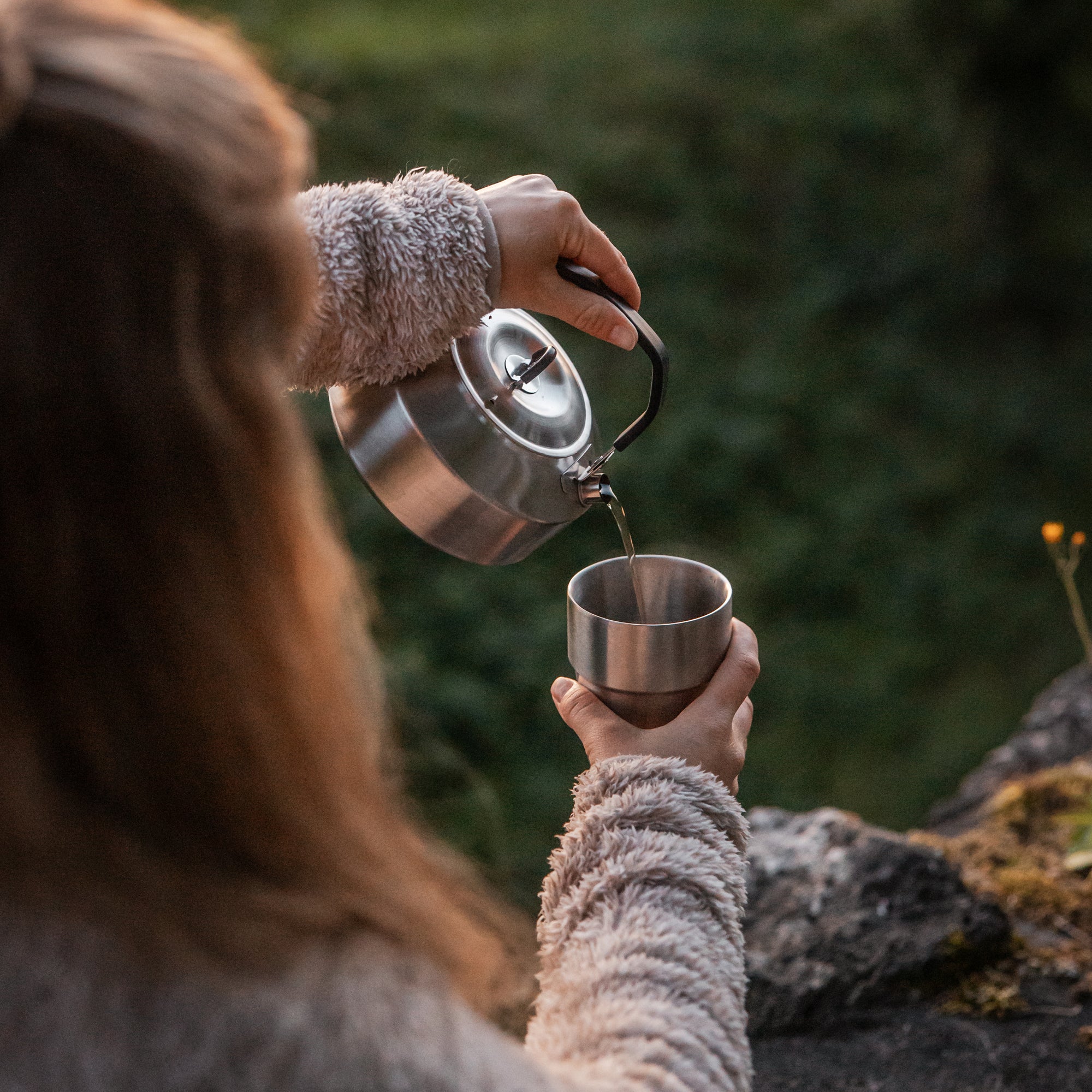 eine Frau schüttet Flüssigkeit aus dem Wasserkessel in den Edelstahl-Trinkbecher 